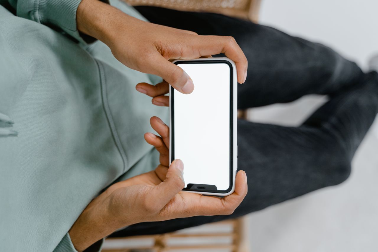 Detailní záběr na ruce držící smartphone s prázdnou obrazovkou, ideální pro digitální mockupy.